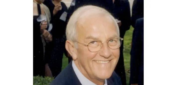 A man with white hair and glasses smiling.