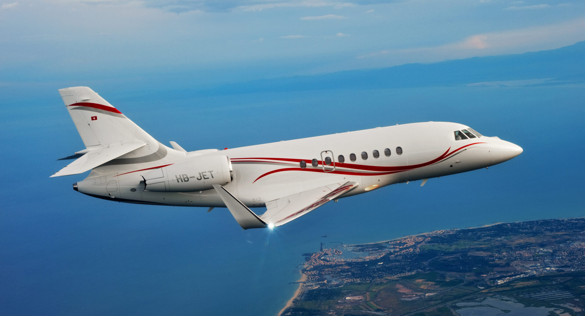 A white jet flying over the ocean with red trim.