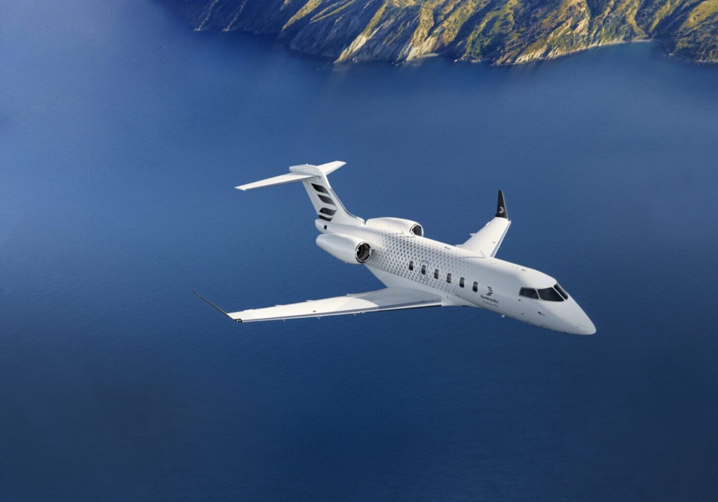 A white airplane flying over the ocean with mountains in the background.