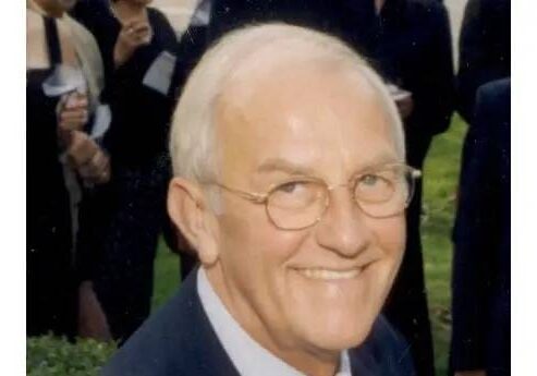 A man with white hair and glasses smiling.